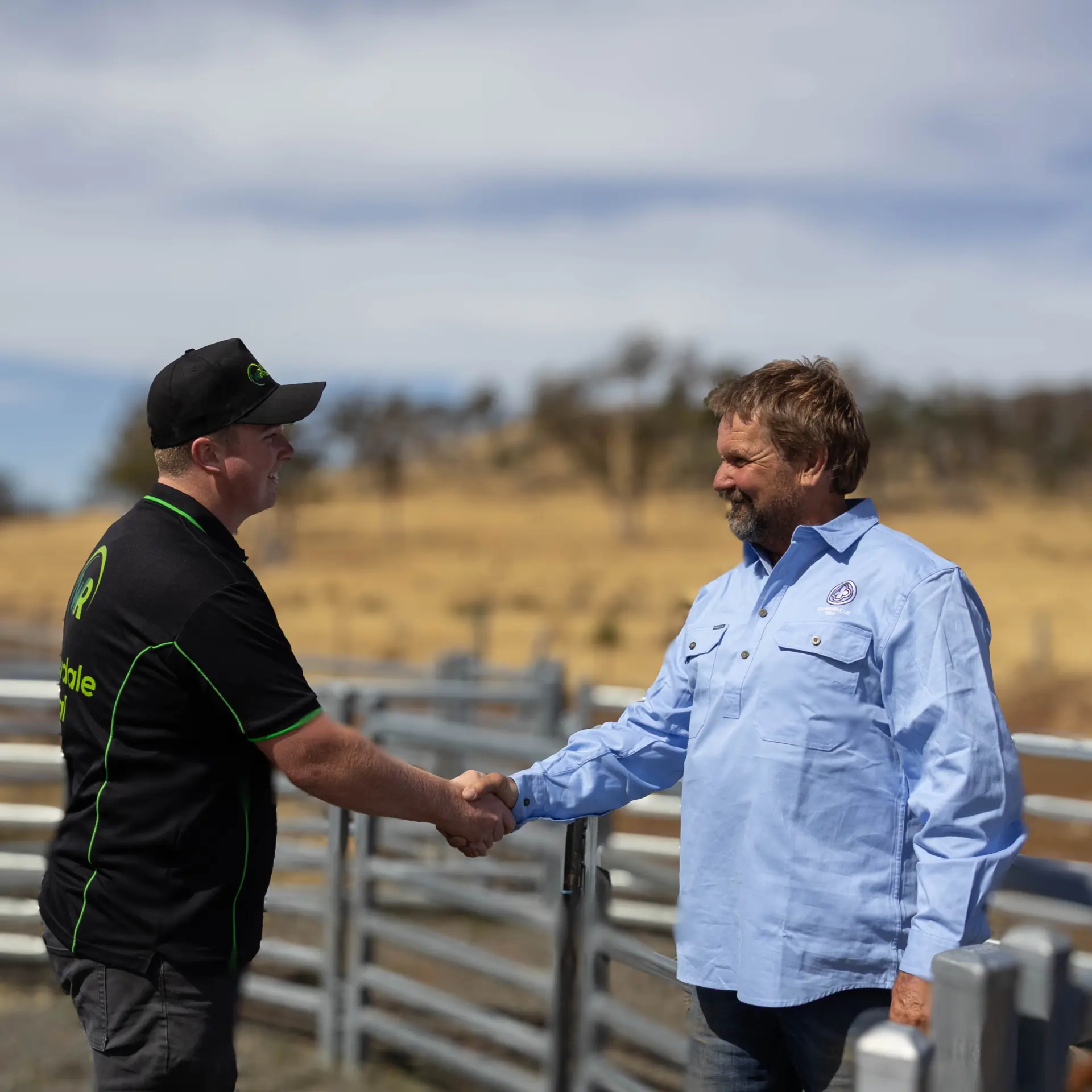 Two men shaking hands at rural farm fence